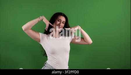 Jeune femme pointant son sourire radieux avec les deux mains sur un écran vert Banque D'Images