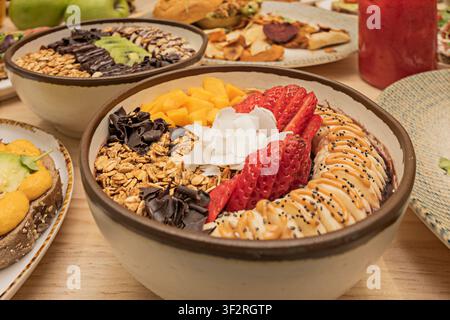Bol Acai vibrant garni de fraises fraîches, mangue, banane, granola, flocons de coco et copeaux de chocolat Banque D'Images