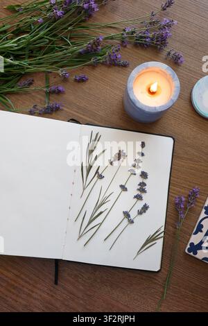 Modèle de maquette de page vierge de cahier ouvert espace de copie texte fond en bois table. Herbier de fleurs de lavande artisanat créatif fait main vue latérale bougie Banque D'Images