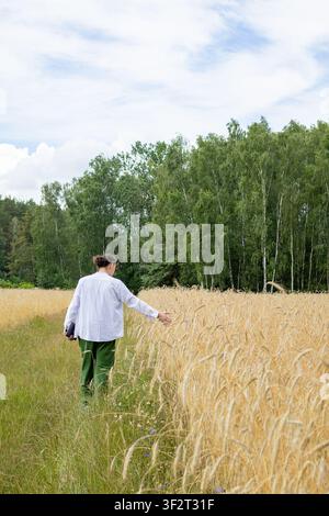 Vue arrière d'un homme d'âge moyen s'éloignant à travers un champ de blé doré les bras tendus sous un ciel d'été. Concept de liberté célébrant la connexion b Banque D'Images