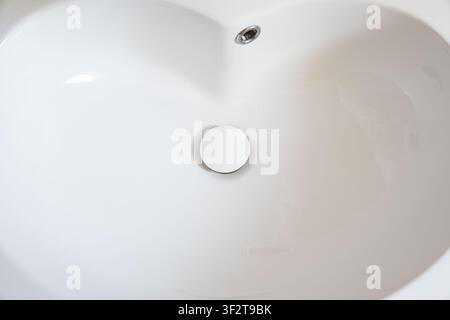 Prise de vue détaillée par le dessus montrant l'intérieur lisse d'un lavabo de salle de bains moderne en céramique blanche, doté d'un bouchon d'évier rétractable et d'une partie métallique sup Banque D'Images