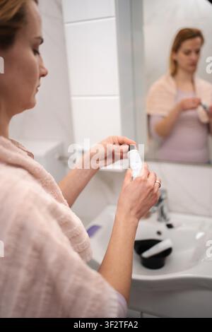 Femme teint ses cheveux à la maison, préparant la teinture pour cheveux, tenant un tube dans ses mains Banque D'Images