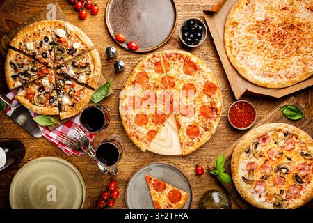 Pizza party en famille ou entre amis. Plats de différents types de pizza et de vin rouge sur une table rustique en bois, vue sur le dessus. Banque D'Images