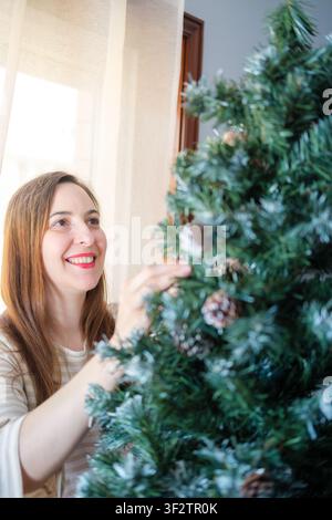 Femme décorant un sapin de Noël avec des ornements d'hiver, profitant de l'esprit des fêtes Banque D'Images