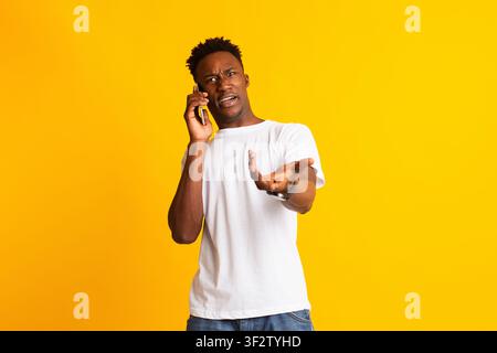 Un gars africain en colère qui parle au téléphone, gestuelle et choquée Banque D'Images