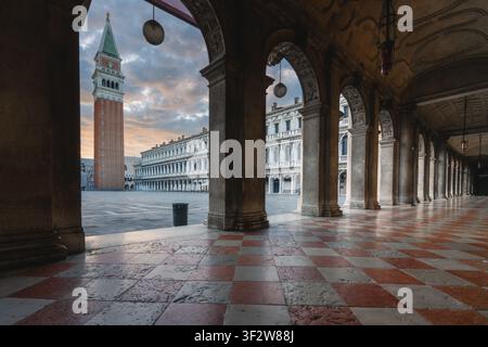 Vue de la place historique Saint-Marc et de l'emblématique Campanile de Saint-Marc vus à travers les arches élégantes des Procuraties Nouvelles au coucher du soleil à Venise Banque D'Images