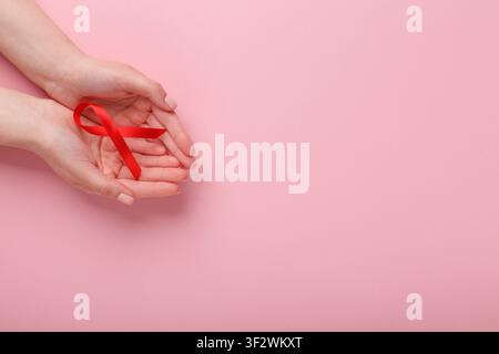 Ruban réaliste rouge de sensibilisation au sida dans les mains sur fond rose Banque D'Images