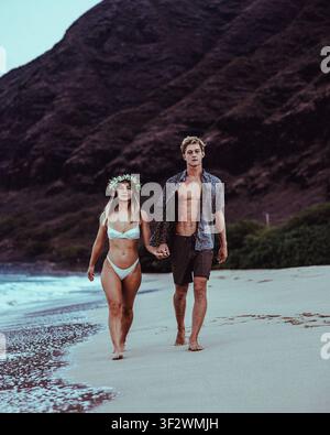 Un jeune couple se détend ensemble sur le sable d'une plage isolée d'Oahu à Hawaï. Banque D'Images