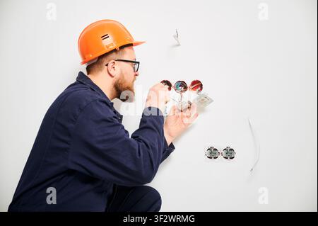 Électricien réparant une prise murale avec un tournevis et des fils apparents. Processus d'installation électrique intérieure lors de la rénovation de la maison, concept de mise en place et de maintenance du système de câblage Banque D'Images