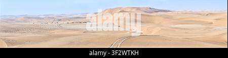 Une vue panoramique large sur les vastes dunes de sable ondulantes et les pistes hors route sinueuses du désert de Namib sous un ciel clair en Namibie. Banque D'Images