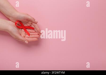 Ruban rouge VIH, SIDA dans les mains sur fond rose Banque D'Images