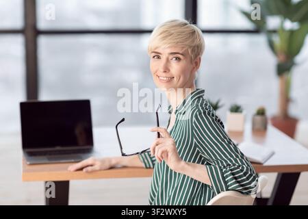 Lady At Laptop Smiling To Camera Posant Dans Le Bureau Moderne Banque D'Images