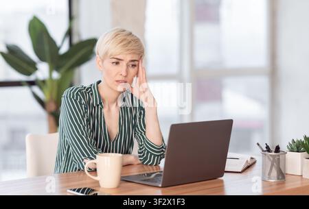 Une Femme Triste Regardant Un Ordinateur Portable Assis Dans Un Bureau Moderne Banque D'Images