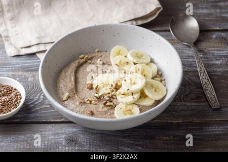 Bouillie de lin saine garnie de tranches de banane, de noix hachées et de graines dans un bol en céramique. Petit déjeuner nutritif avec des ingrédients naturels, copie Banque D'Images