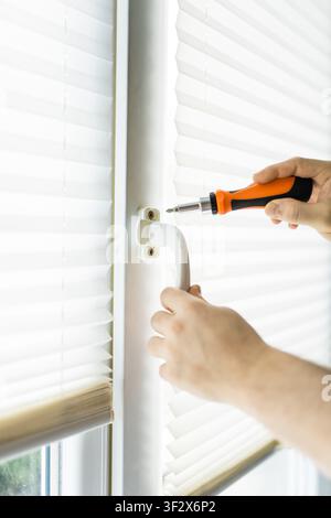 Close up d'un bricoleur utilisant un tournevis orange pour réparer ou remplacer une poignée de fenêtre en plastique blanc Banque D'Images