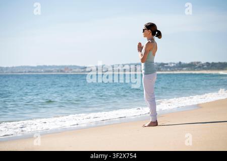 Femme pratiquant la méditation yoga sur une plage ensoleillée Banque D'Images