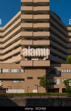 Niché le long d'un canal tranquille à Nakameguro, Tokyo, ce bâtiment résidentiel moderne présente un design étagé frappant. Le béton beige et la brique Banque D'Images