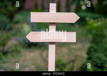 Panneau directionnel en bois vierge avec des flèches pointant à gauche et à droite dans un jardin vert. Un panneau en bois vide avec deux flèches opposées sur un fond vert flou Banque D'Images