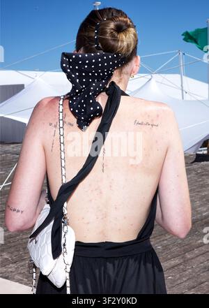 Vue arrière d'une jeune femme adulte portant une robe noire dos nu exposant divers tatouages, écharpe à pois nouée autour de ses cheveux Banque D'Images