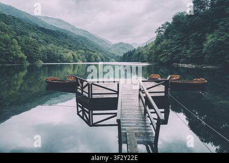 Lac Biogradsko serein reflétant des montagnes de forêt luxuriante, avec une jetée en bois et des bateaux à louer, créant une scène naturelle paisible au Monténégro Banque D'Images