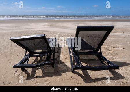 deux chaises longues noires vides sur une plage de sable Banque D'Images