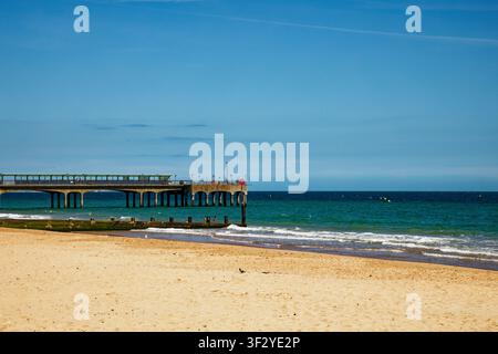Une plage de sable déserte avec brise-lames et jetée en arrière-plan avec une mer bleu-vert et un ciel bleu, Boscombe Pier, Bournemouth, Dorset, Angleterre. Banque D'Images
