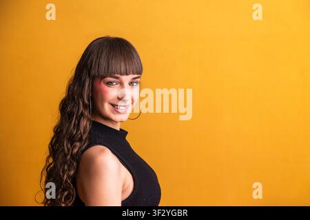 Jeune femme souriant avec assurance sur un fond jaune éclatant Banque D'Images