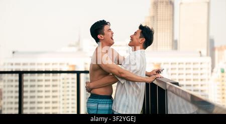 Couple gay riant et s'embrassant sur le toit, profitant de la vie urbaine et de la complicité Banque D'Images