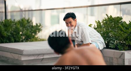 Homme asiatique souriant à son partenaire qui prend une photo, couple gay profitant de la piscine sur le toit Banque D'Images