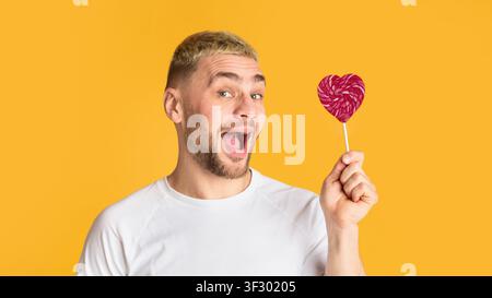 Homme émotionnel avec la bouche ouverte tient coeur lollipop Banque D'Images