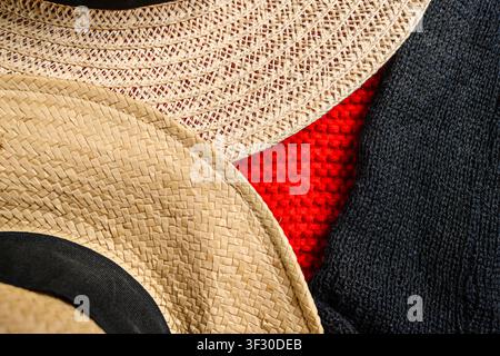 Vue rapprochée abstraite montrant des textures contrastées de chapeaux de paille, d'un pull tricoté rouge vif et d'un tissu tissé noir. Idéal pour la mode, les textiles, a Banque D'Images