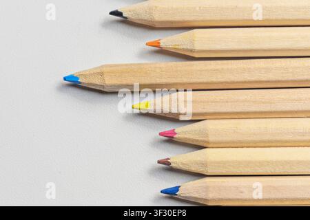 Un plan rapproché en hauteur d'un groupe de crayons de couleur naturelle en bois avec des pointes de différentes couleurs, disposés en rangée sur un fond en papier texturé blanc Banque D'Images