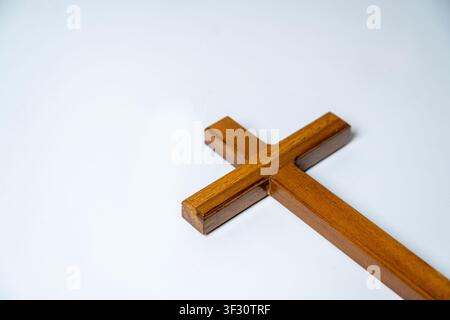 Une photographie en contre-plongée en studio d'une simple croix chrétienne en bois poli positionnée en diagonale sur un fond blanc uni. Cette image minimaliste r Banque D'Images