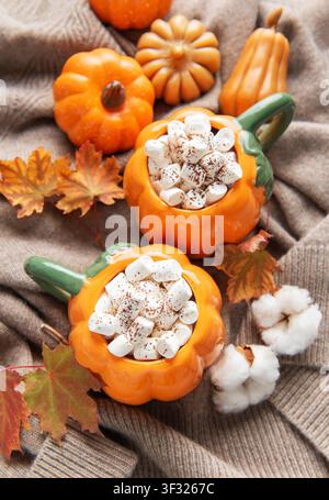 Deux mugs chauffants en forme de citrouille remplis de cacao et de guimauves sur un pull confortable avec un décor d'automne Banque D'Images