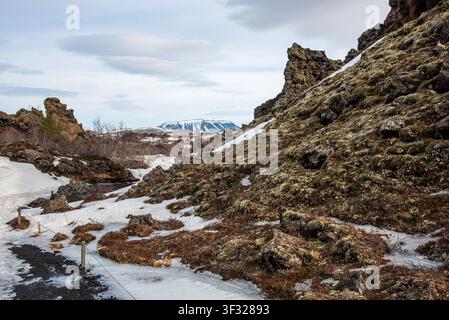 Un sentier de randonnée bordé de cordes serpente à travers d'imposants rochers de lave recouverts de mousse et de plaques de neige. En arrière-plan, encadré par les formations volcaniques sombres, Banque D'Images