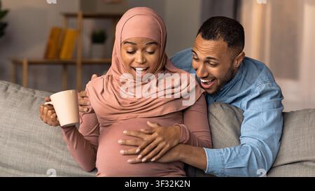 Femme afro-américaine enceinte heureuse et homme touchant avec enthousiasme le ventre à la maison Banque D'Images