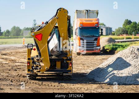 Machines de terrassement industrielles mettant en vedette un godet de pelleteuse jaune et un camion-benne orange lourd sur une zone de construction Banque D'Images