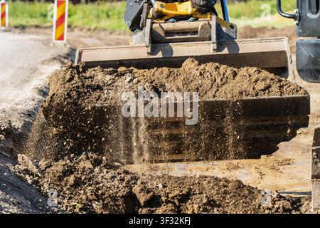 Vue avant détaillée d'un large godet en acier déversant des matériaux de remblai en vrac sur un chantier de fouille de sous-sol actif Banque D'Images
