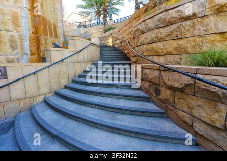 Los Angeles, Californie – 25 janvier 2026 : Un escalier en pierre incurvé s’élève entre des murs de grès texturés avec des rampes en métal noir élégantes Banque D'Images