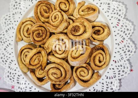 Brioches à la cannelle fraîchement cuites disposées sur une assiette blanche à bordure en dentelle Banque D'Images