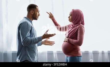 Couple se disputant, femme enceinte portant un hijab et homme exprimant de l'inquiétude, cadre domestique Banque D'Images