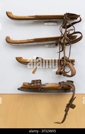 Battes de glace en bois vintage avec lanières en cuir et lames en métal exposées sur un mur blanc à IJlst, Friesland, Pays-Bas, évoquant la nostalgie, l’artisanat Banque D'Images