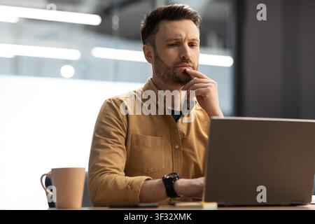 Homme caucasien ciblé travaillant sur ordinateur portable dans le bureau moderne, concept d'entreprise Banque D'Images