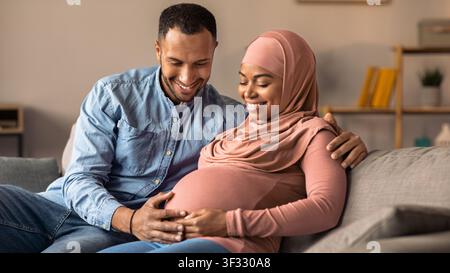Femme noire enceinte heureuse et son partenaire souriant ensemble, attendant l'arrivée du bébé à la maison Banque D'Images