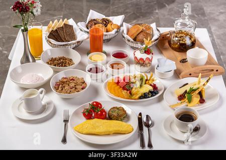 Table de brunch luxueuse avec omelette, tomates, pâtisseries, fruits et thé Banque D'Images