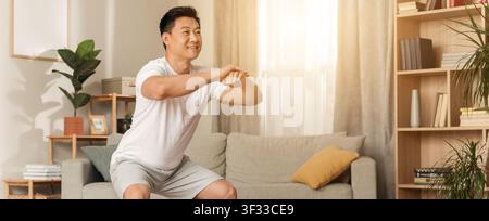 Homme asiatique souriant faisant de l'exercice à la maison, effectuant des squats dans un salon moderne, concept de fitness Banque D'Images