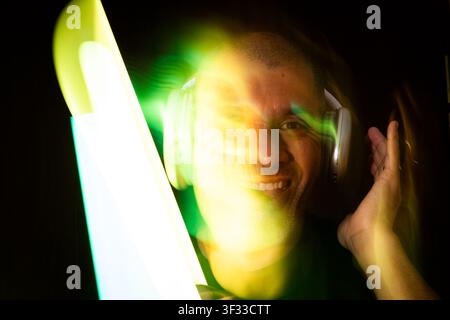 Homme souriant, écoutant de la musique avec un casque, entouré de traînées de lumière colorées Banque D'Images
