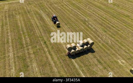 Vue aérienne d'un tracteur avec chargeur frontal ramassant des balles de foin rondes dans un champ récolté, Sesto Ulteriano, Lombardie, Italie. Banque D'Images