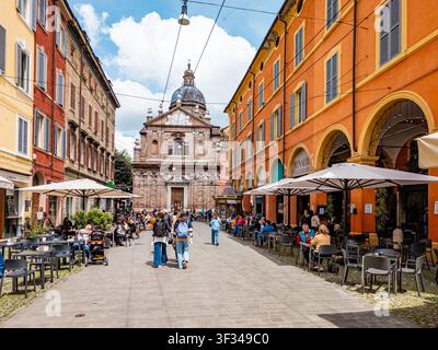 Des piétons marchent le long d'une charmante rue piétonne à Modène, en Italie, bordée de bâtiments colorés et de cafés en terrasse animés où les gens profitent d'un verre Banque D'Images