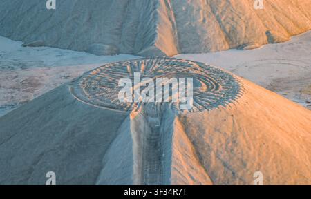 Vue aérienne de motifs radiaux complexes d'excavation creusés dans un tas de sable circulaire par des machines lourdes sous une lumière chaude de l'heure dorée, France. Banque D'Images